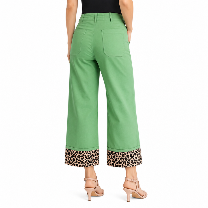 A model is shown from the back wearing green cropped wide-leg pants with a leopard print cuff, paired with a black top and beige high-heeled sandals, against a plain white background.