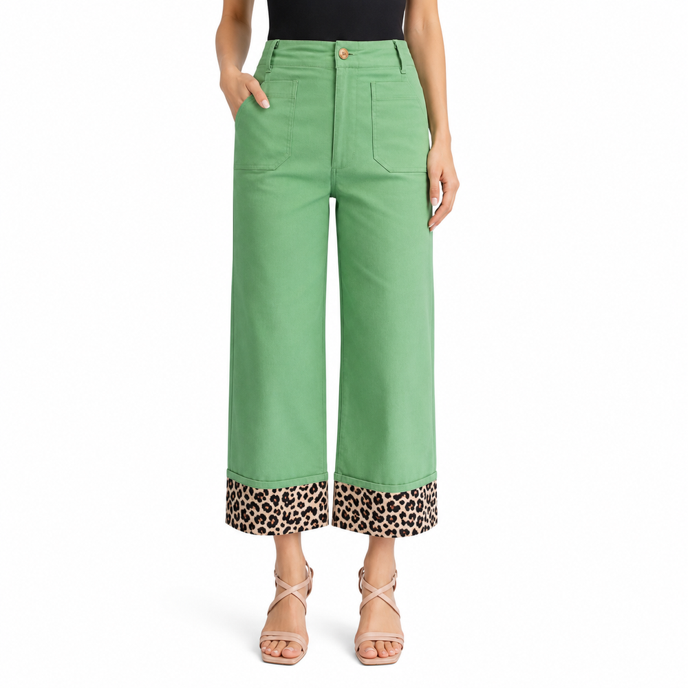 A model is wearing a pair of sage green cropped wide-leg pants with a leopard print trim at the hem, paired with a black top and beige strappy heels against a white background.