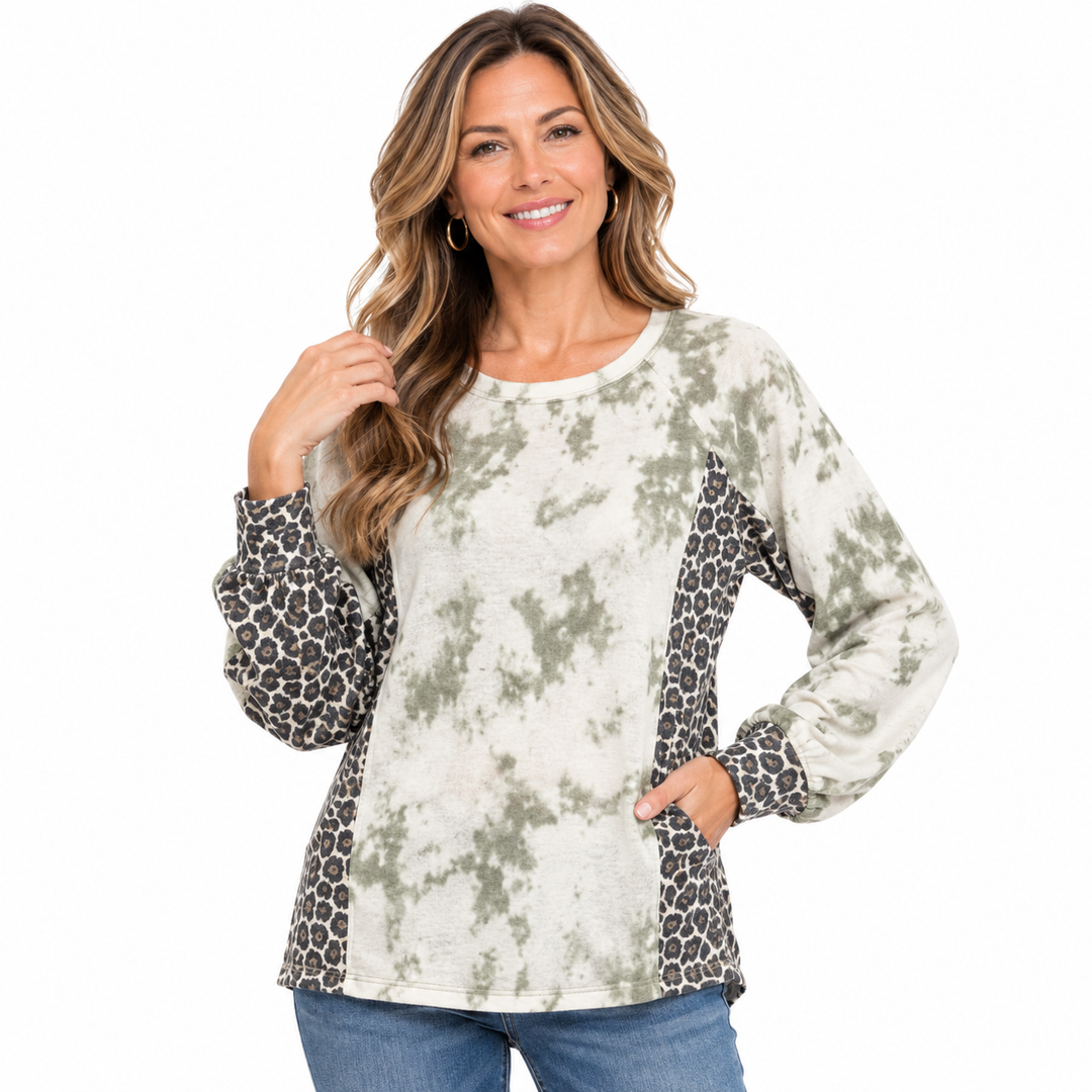 A woman modeling a long-sleeve top with a distressed tie-dye pattern in sage green and cream, featuring leopard-print side panels and cuffs, paired with blue jeans against a plain white background.