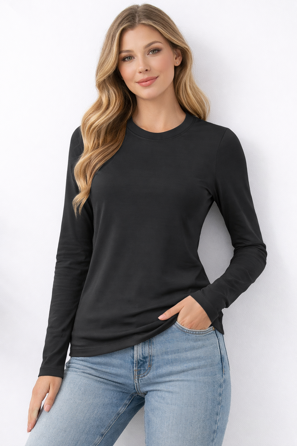 Woman wearing a black long-sleeve top and blue jeans against a white background