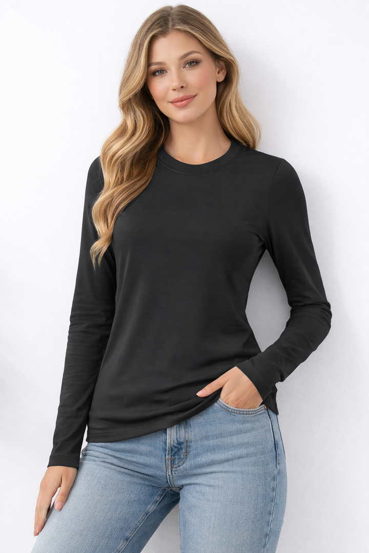 Woman wearing a black long-sleeve top and blue jeans against a white background