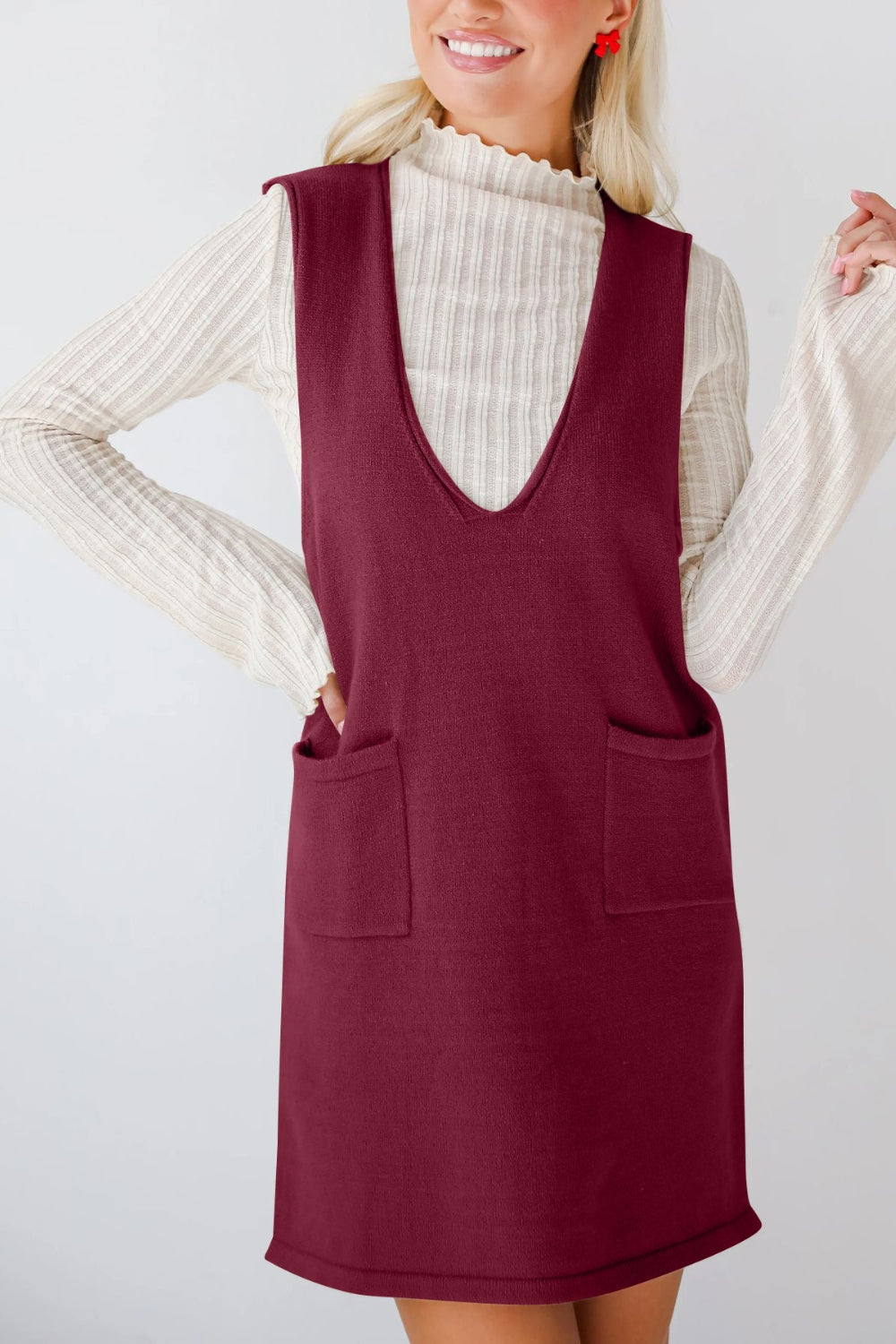 Woman wearing a burgundy dress over a cream sweater on a white background