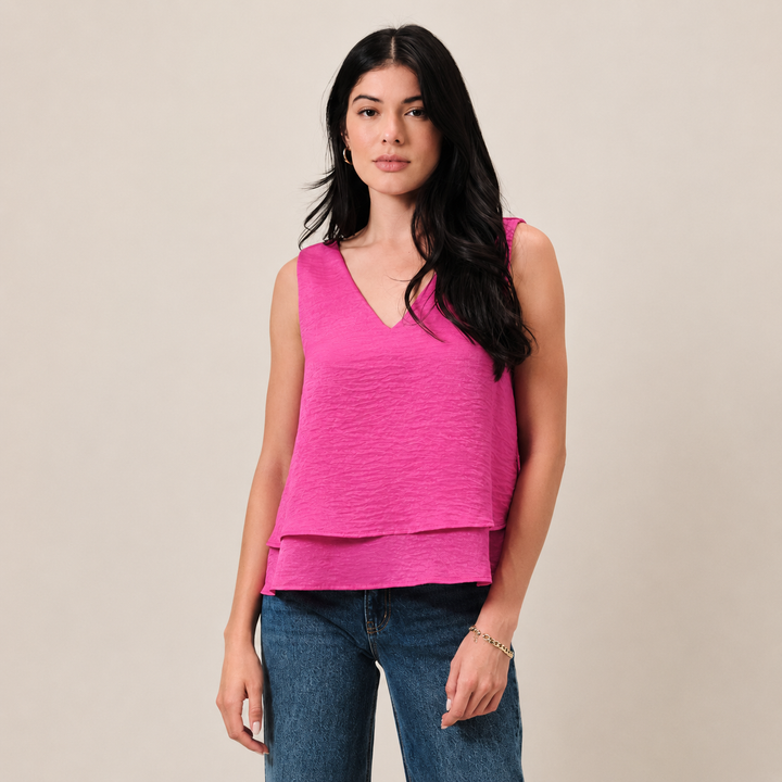 Woman wearing a bright pink sleeveless top and blue jeans against a beige background