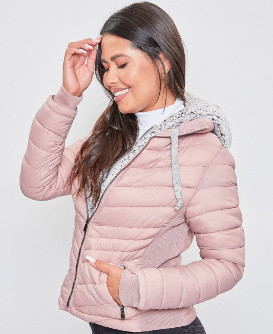 Woman wearing a pink quilted jacket with a white hood against a light gray background