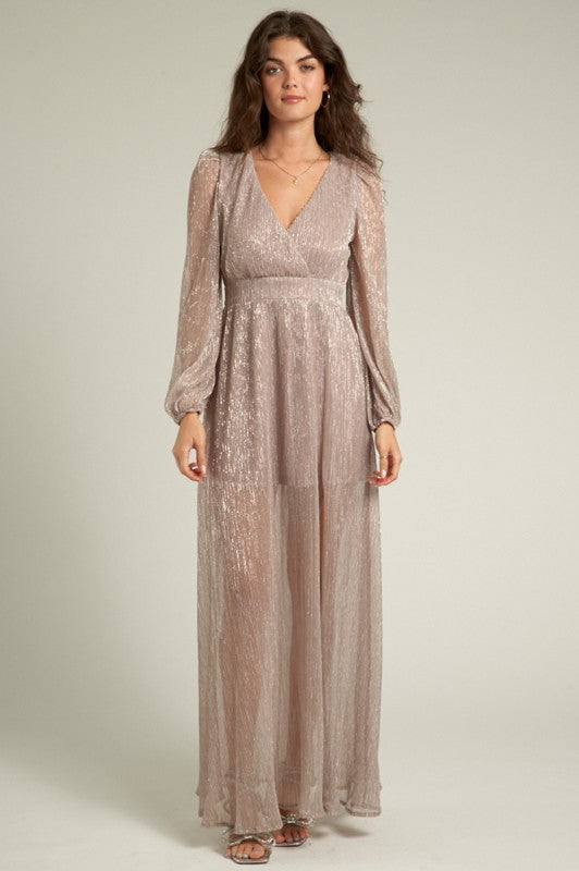 Woman wearing a long, sheer, patterned dress against a neutral background