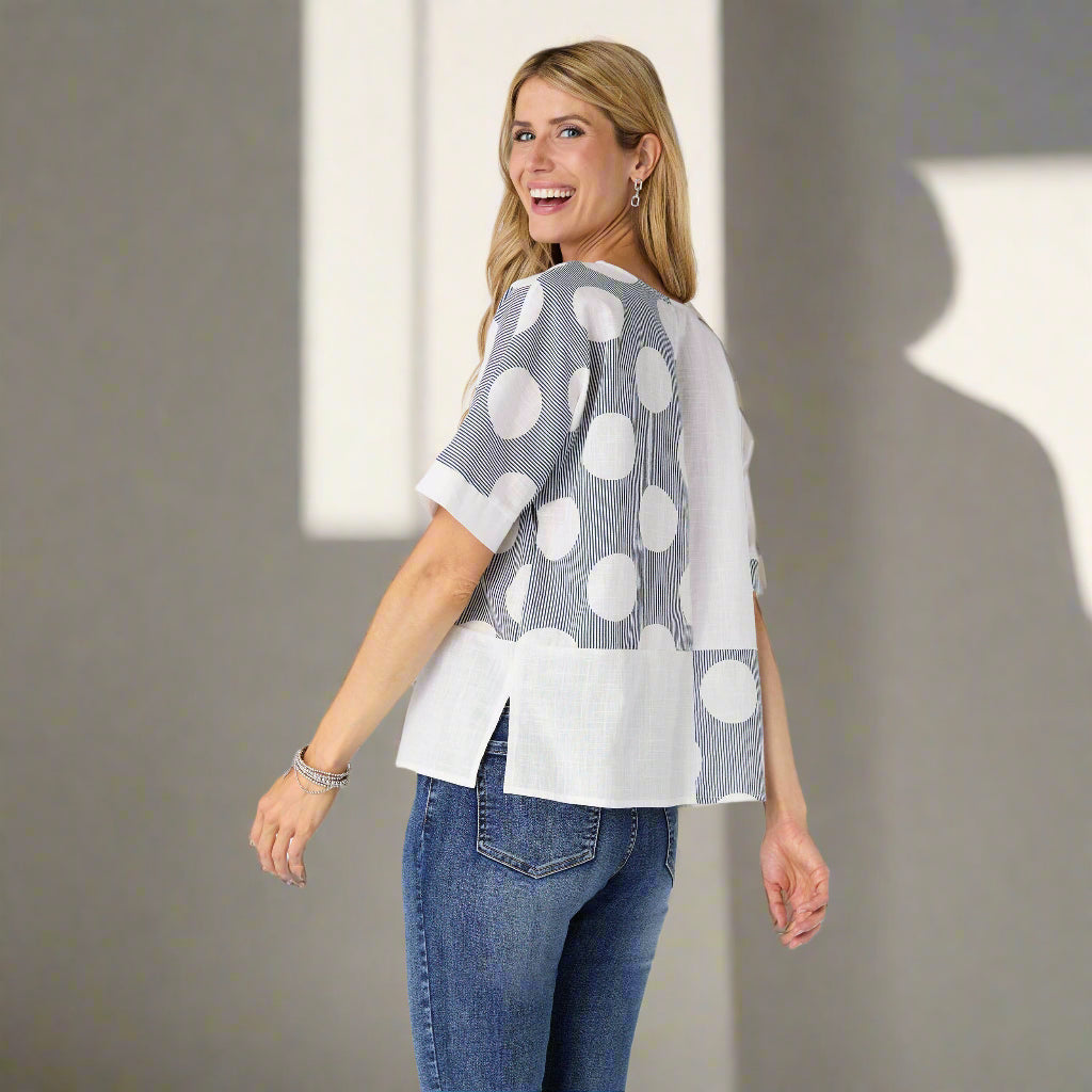Woman wearing a gray and white polka dot top with blue jeans on a plain background