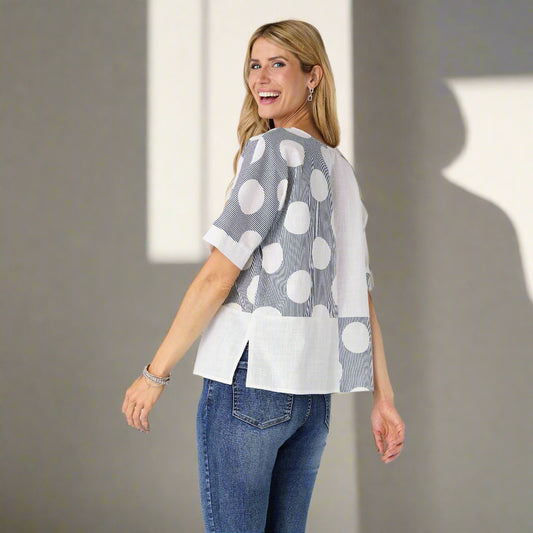 Woman wearing a gray and white polka dot top with blue jeans on a plain background