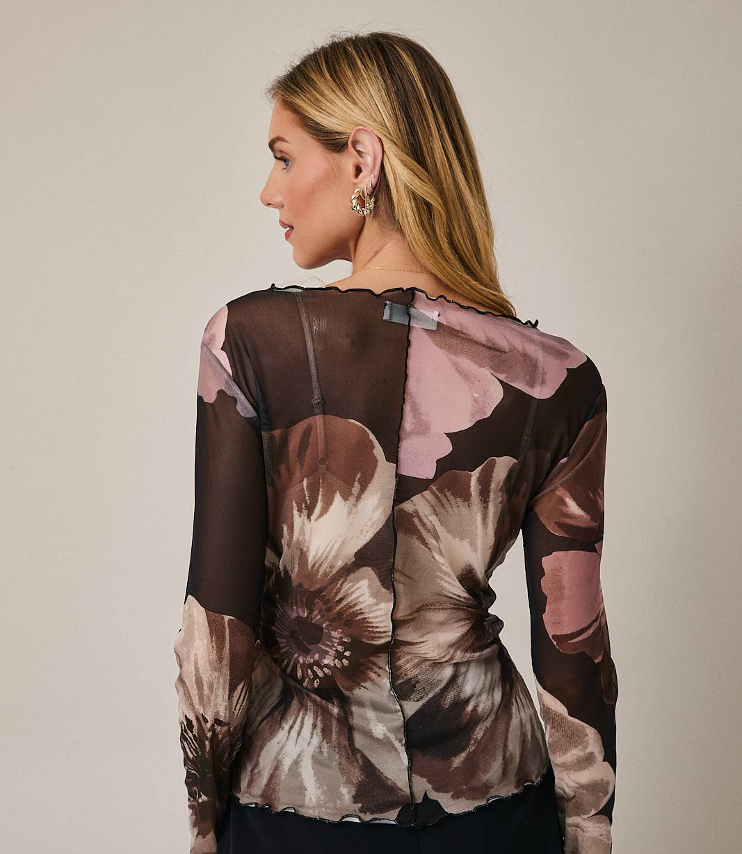 Woman wearing a floral sheer top with a plain background