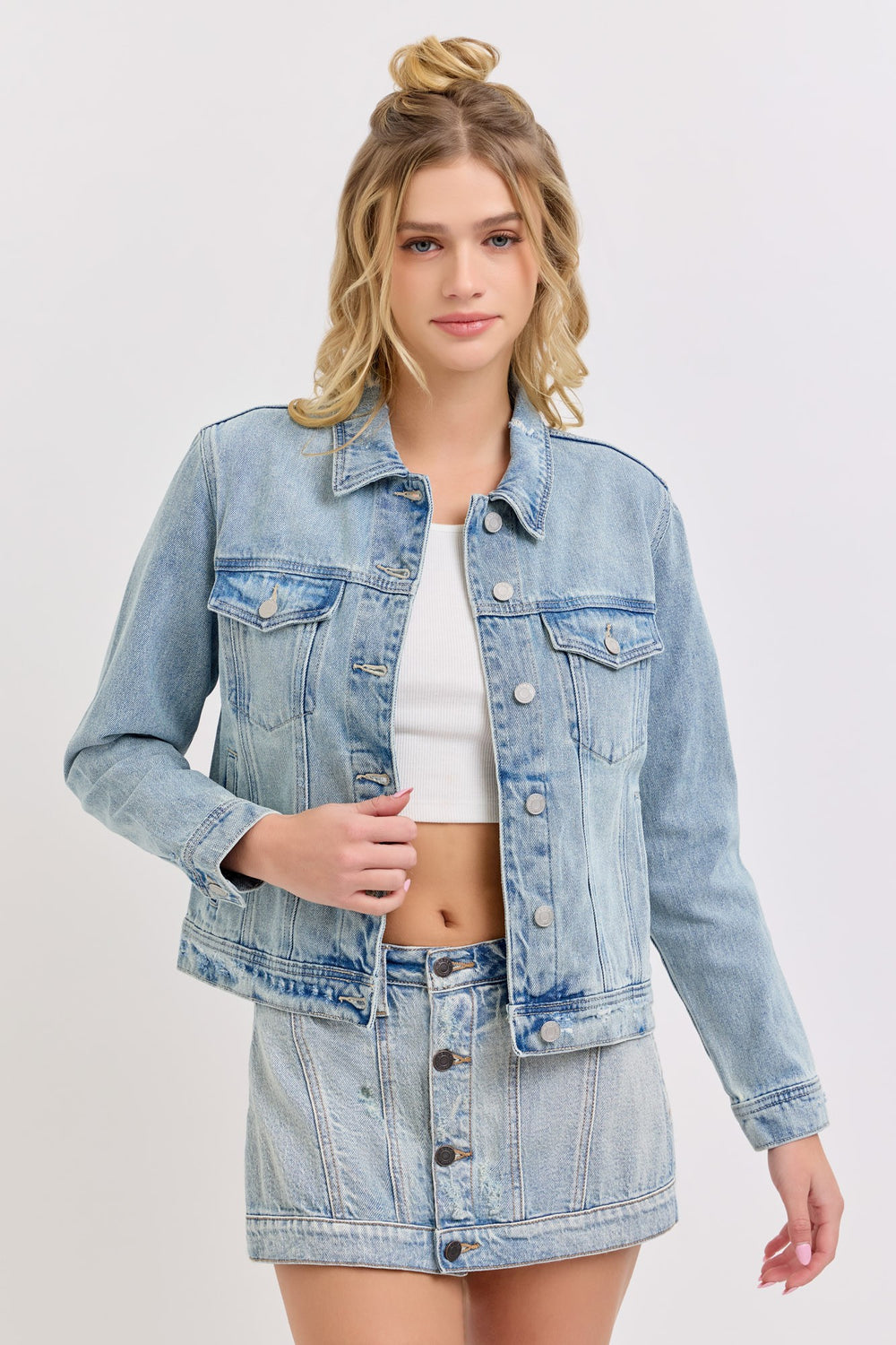 Woman wearing a light blue denim jacket over a white top on a plain background