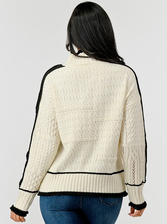 Woman wearing a cream sweater with black accents on a plain background