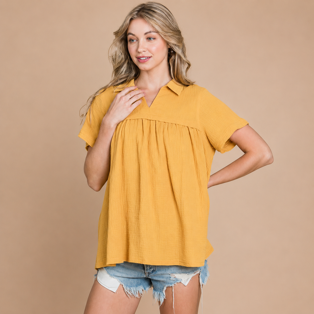 Woman wearing a mustard yellow blouse and denim shorts on a beige background