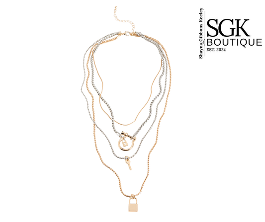Stack of gold and silver necklaces on a white background with SGK Boutique branding.