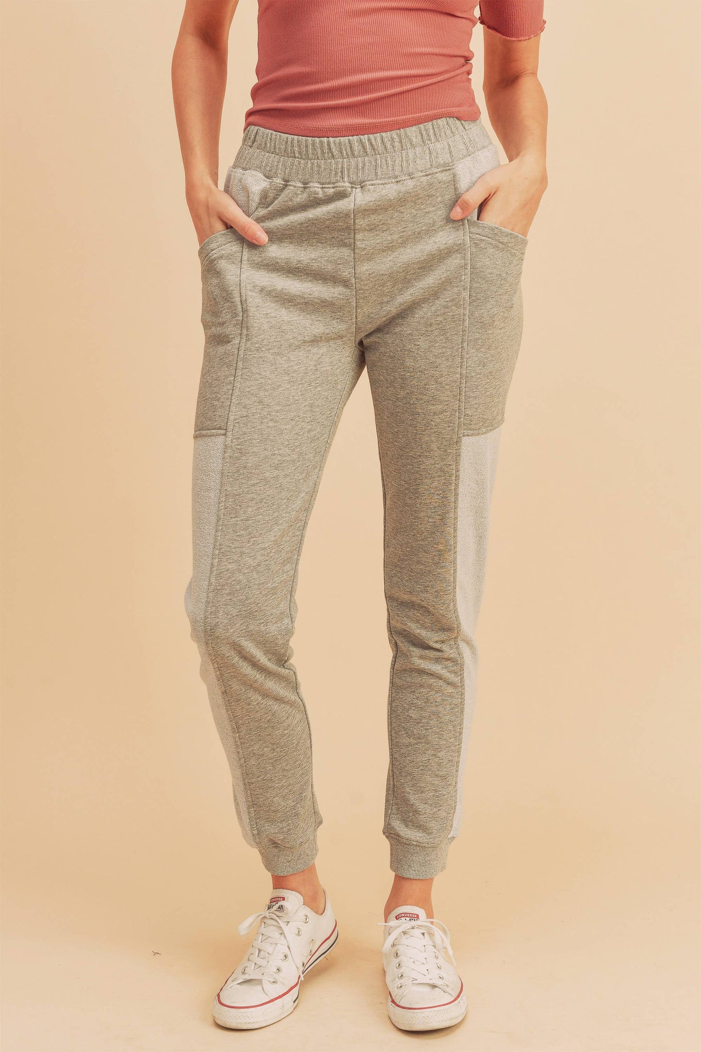 Person wearing gray jogger pants and a pink top on a beige background