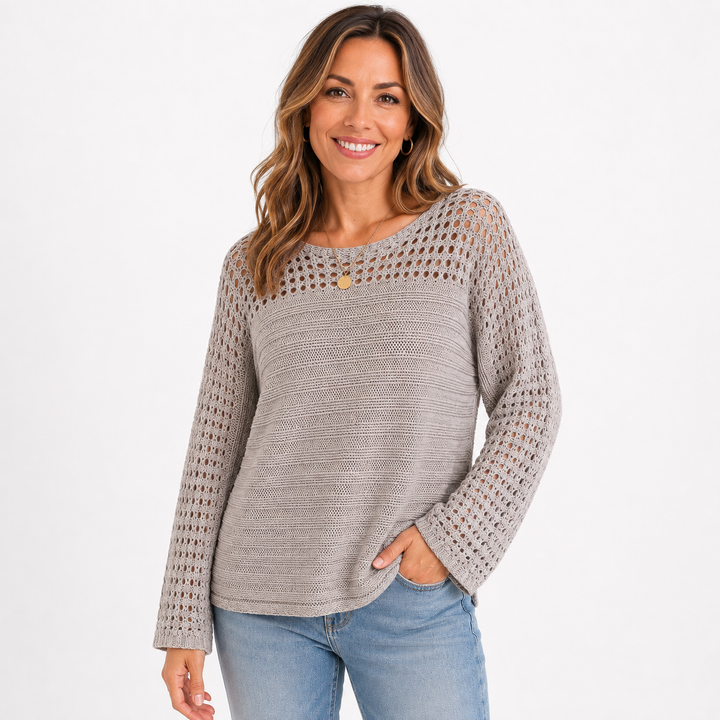 A woman wearing a light gray knit sweater with an open-knit yoke and long sleeves, paired with blue jeans, against a plain white background.