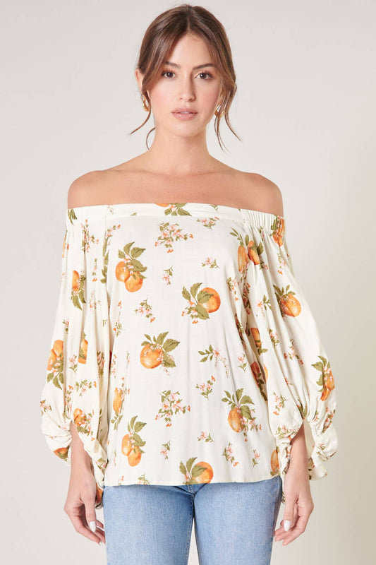 Woman wearing a floral off-shoulder top with orange patterns on a plain background