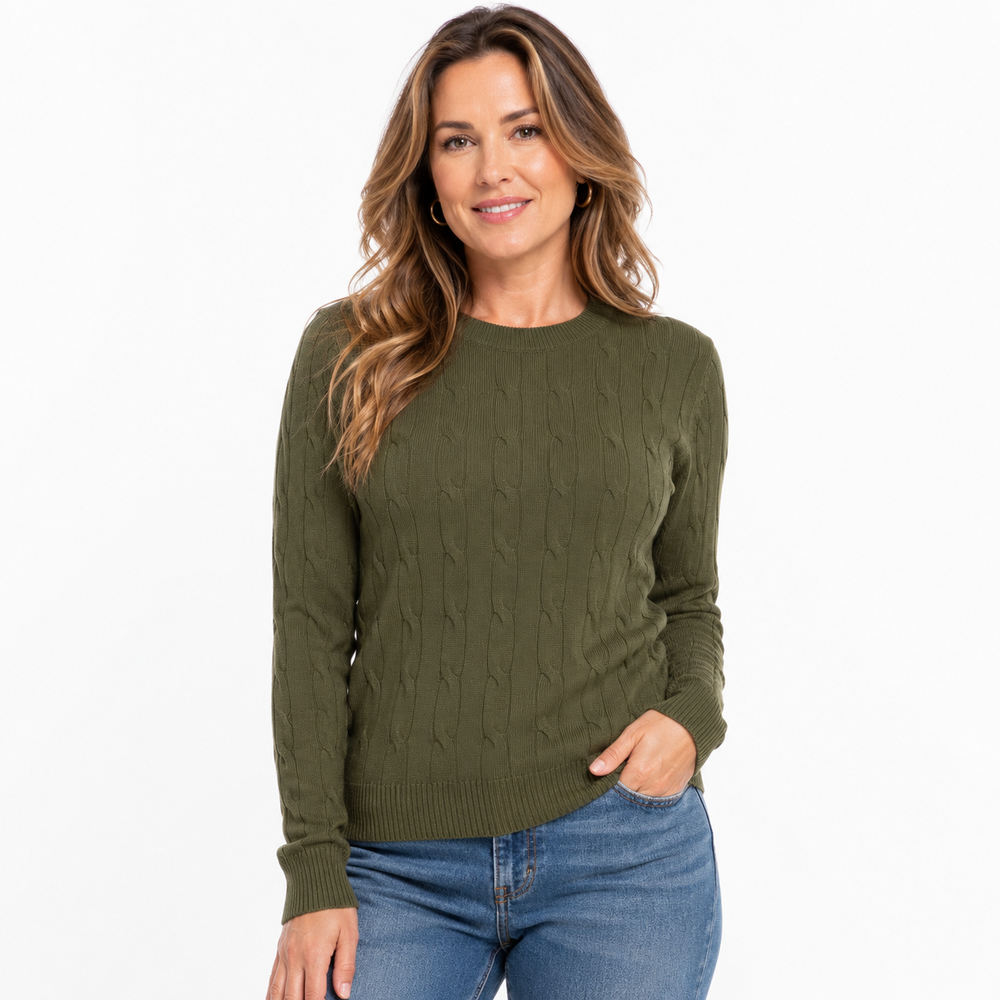 A woman wearing an olive green cable-knit crewneck sweater and blue jeans, standing against a plain white studio background.