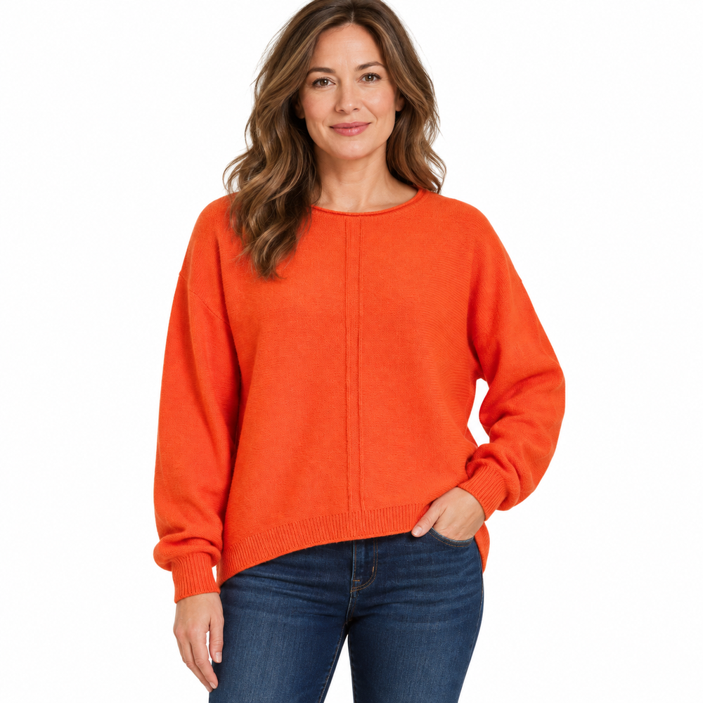 A woman wearing a bright orange knit sweater with a crew neck and ribbed cuffs, paired with dark blue jeans, photographed against a solid white background.