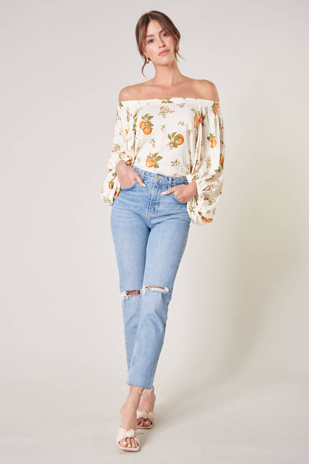 Woman wearing a floral off-shoulder top and light blue jeans on a white background