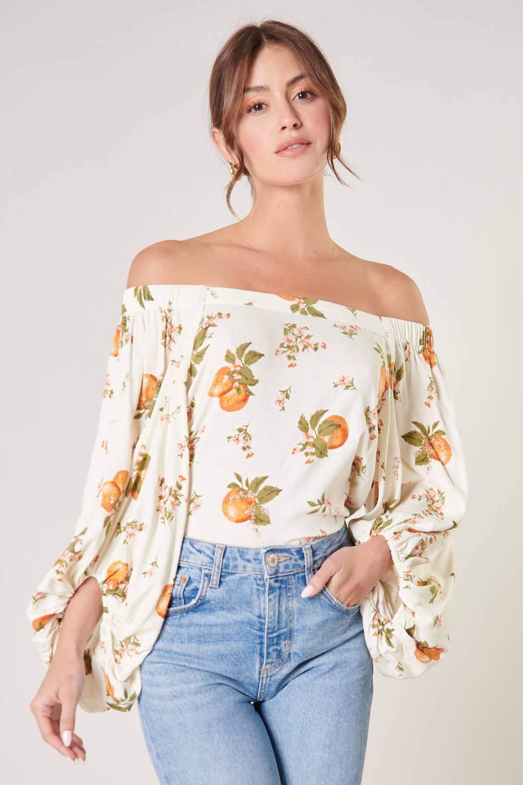 Woman wearing a floral off-shoulder top and blue jeans on a plain background
