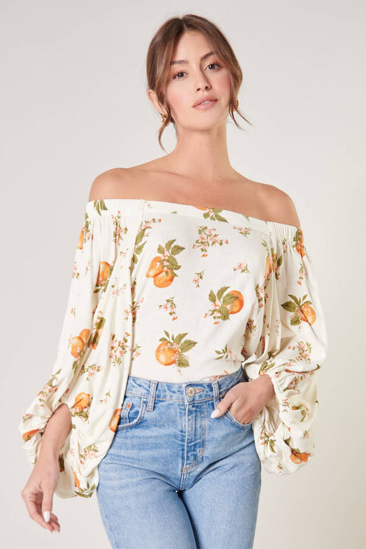 Woman wearing a floral off-shoulder top and blue jeans on a plain background