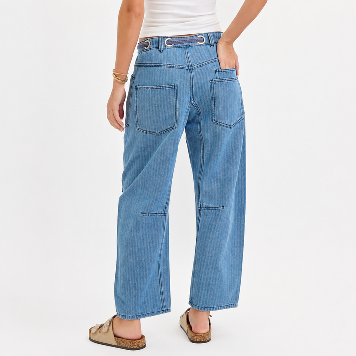 A model shown from the back wearing light blue denim wide-leg cropped pants with vertical pinstripes, a white top, and tan slide sandals, set against a plain white studio background.
