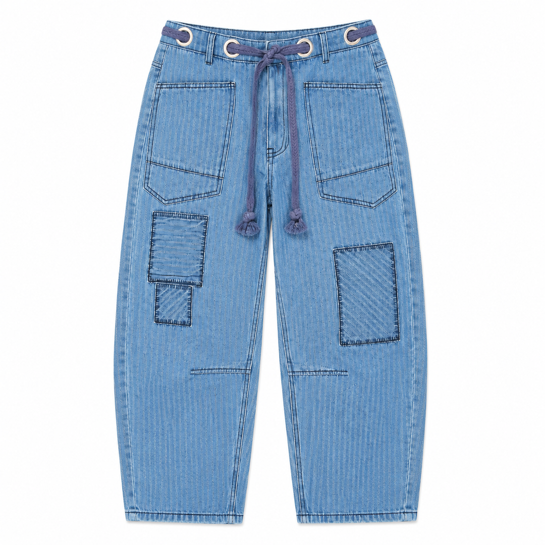 Light blue denim pants featuring a drawstring waist, decorative metal grommets, and large patchwork-style pockets on the front and legs, shown against a plain white background.