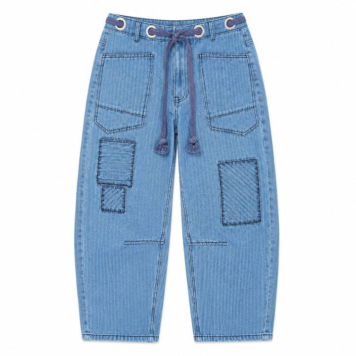 Light blue denim pants featuring a drawstring waist, decorative metal grommets, and large patchwork-style pockets on the front and legs, shown against a plain white background.