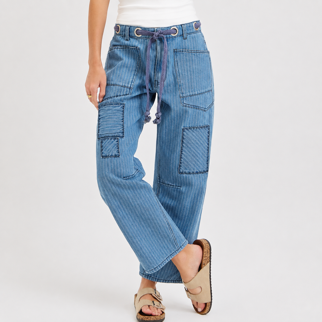 A person wearing light blue denim patchwork pants with a drawstring waist, shown from the waist down against a plain light gray studio background.