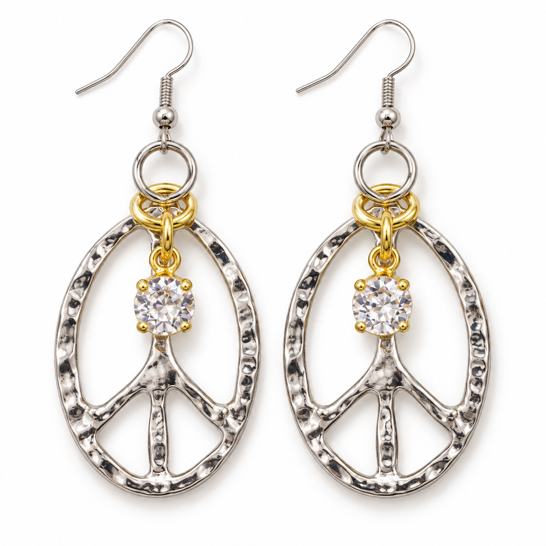 A pair of silver and gold drop earrings featuring a hammered oval peace sign design with a clear round-cut cubic zirconia gemstone at the center of each earring, suspended from silver fishhook wires on a white background.