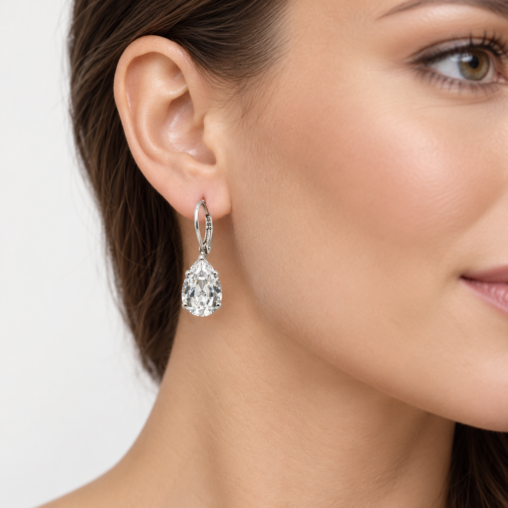 A close-up of a woman's ear and side profile wearing a silver-tone hoop earring with a pear-cut clear gemstone drop.