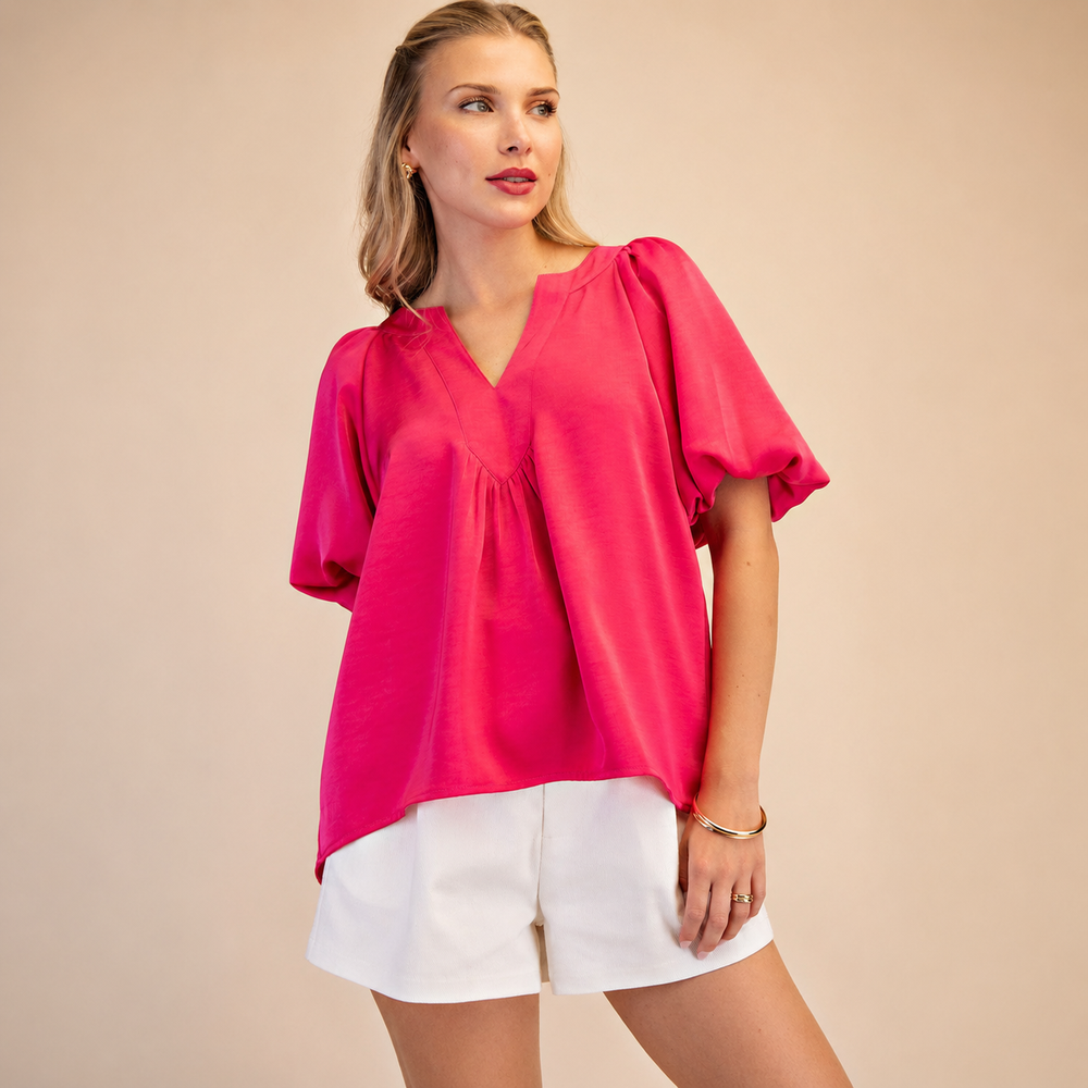 Woman wearing a bright pink blouse and white shorts against a beige background