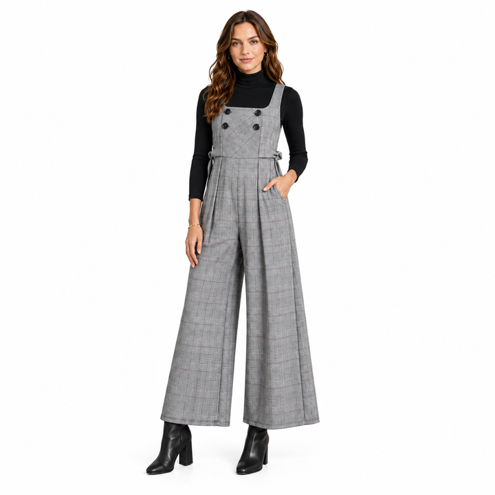 A woman modeling a gray plaid wide-leg jumpsuit with double-breasted buttons, worn over a black long-sleeve turtleneck and black ankle boots, on a solid white background.