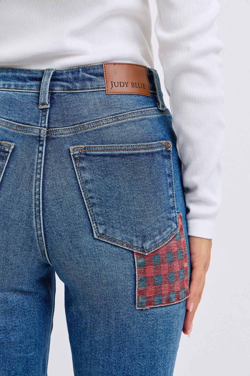 Blue jeans with a plaid patch on the back pocket, worn by a person.