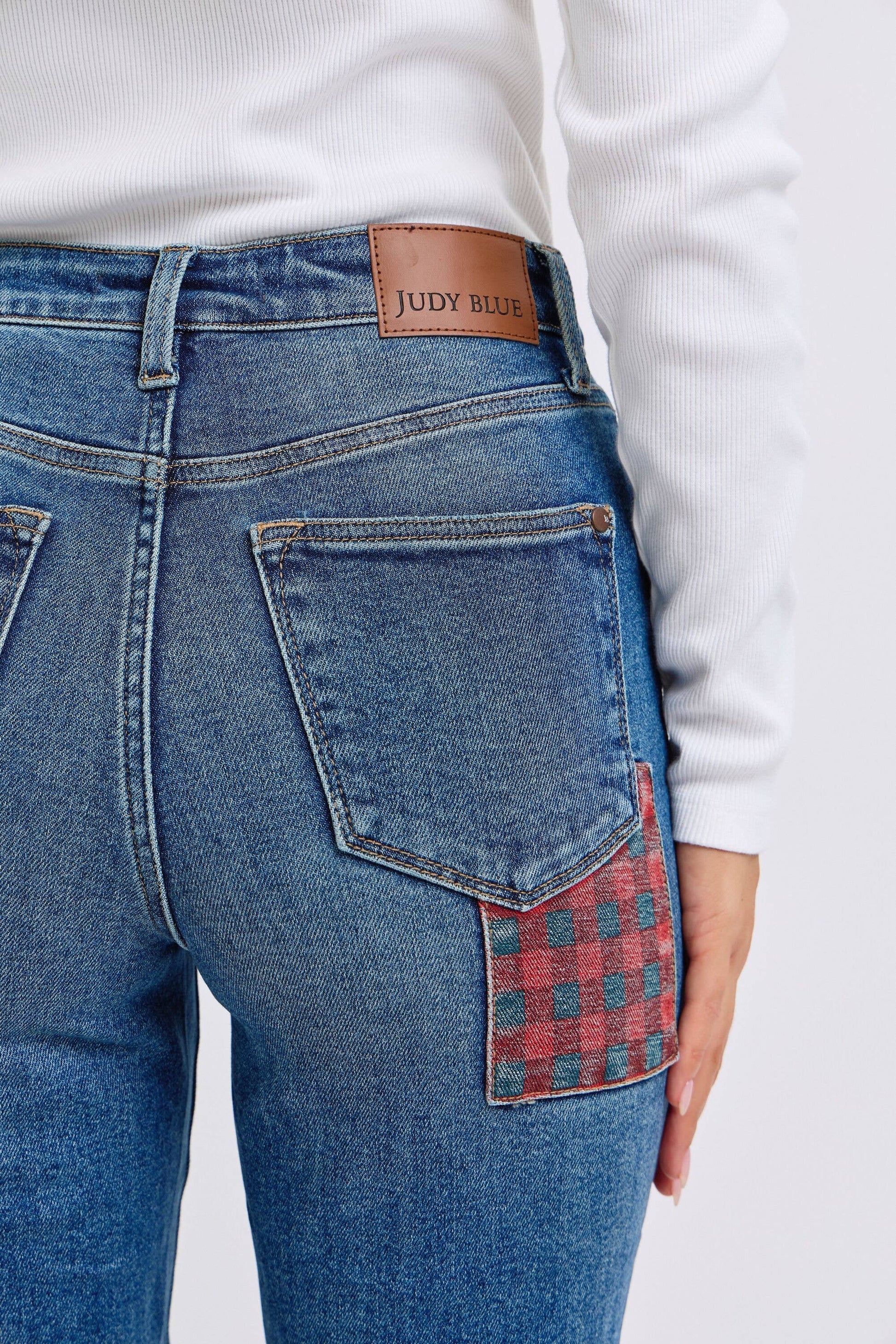Blue jeans with a plaid patch on the back pocket, worn by a person.