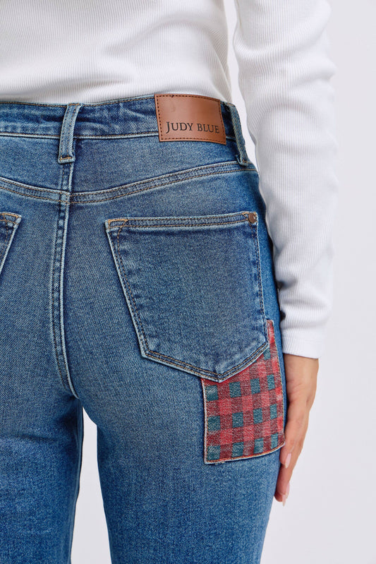 Blue jeans with a plaid patch on the back pocket, worn by a person.