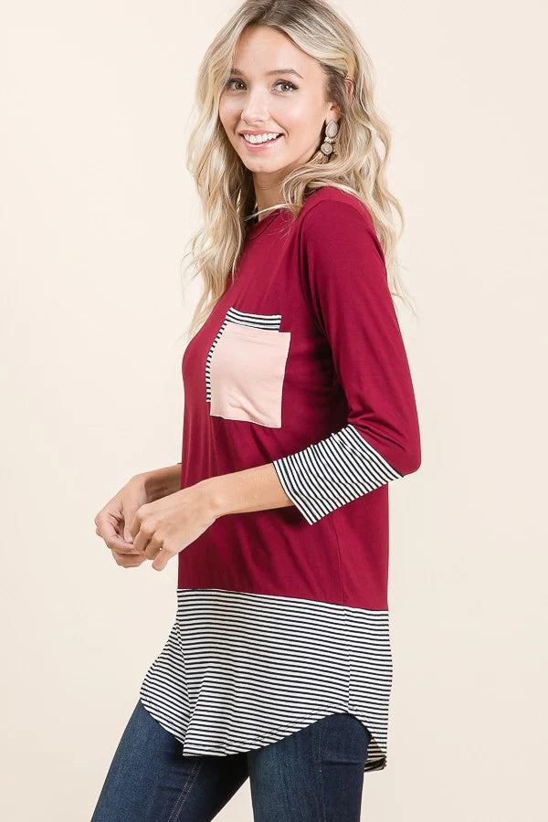 Woman wearing a burgundy top with a pink pocket and striped hem on a beige background