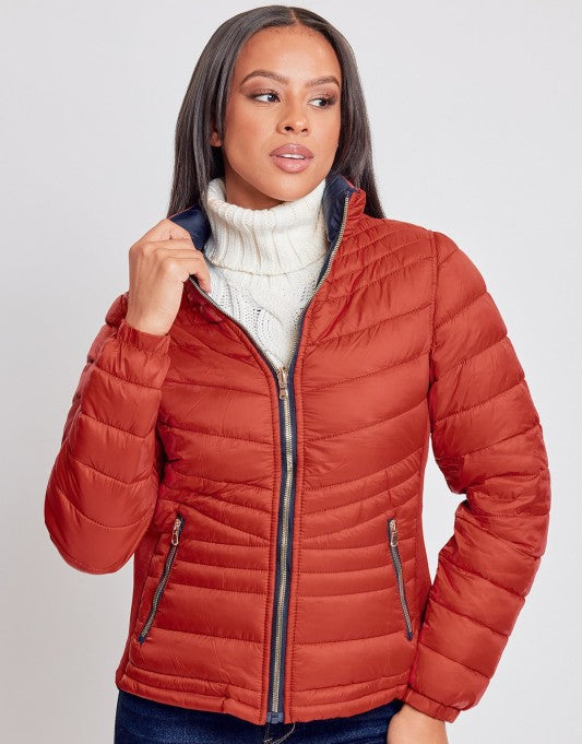 Woman wearing a orange puffer jacket over a white turtleneck on a light gray background