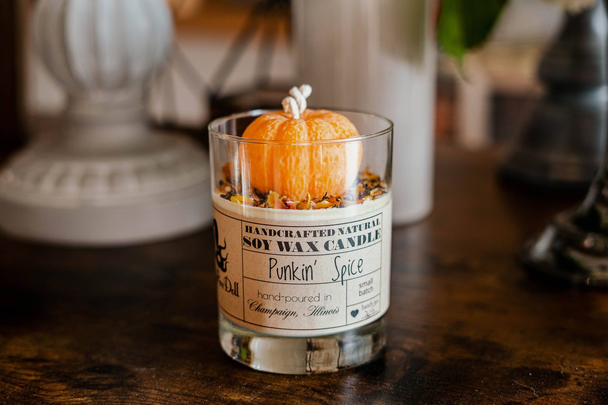 Handcrafted natural soy wax candle with a pumpkin decoration on a wooden surface.