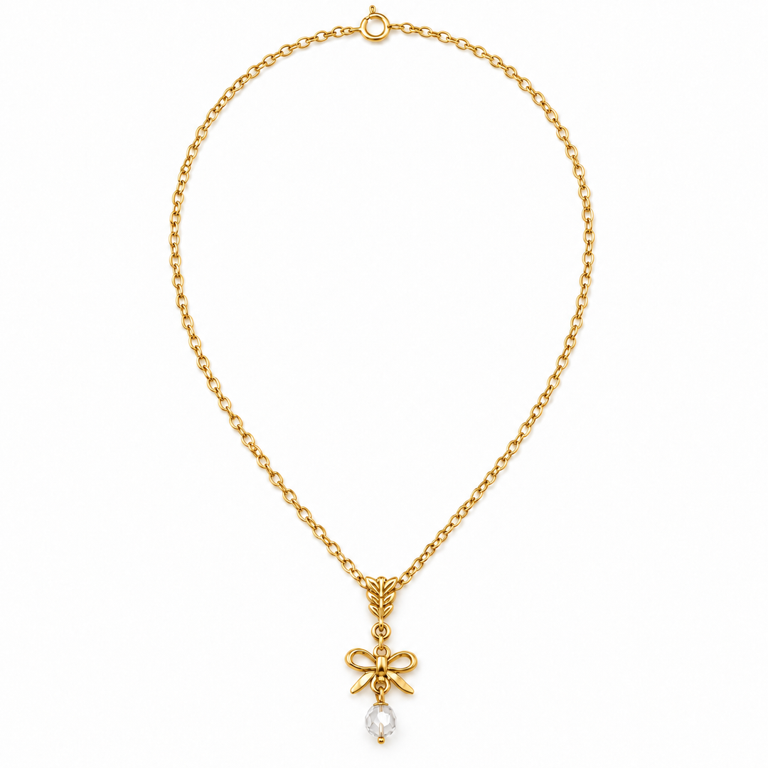 A gold chain necklace with a bow-shaped pendant and a small clear teardrop gemstone, shown on a plain white background.