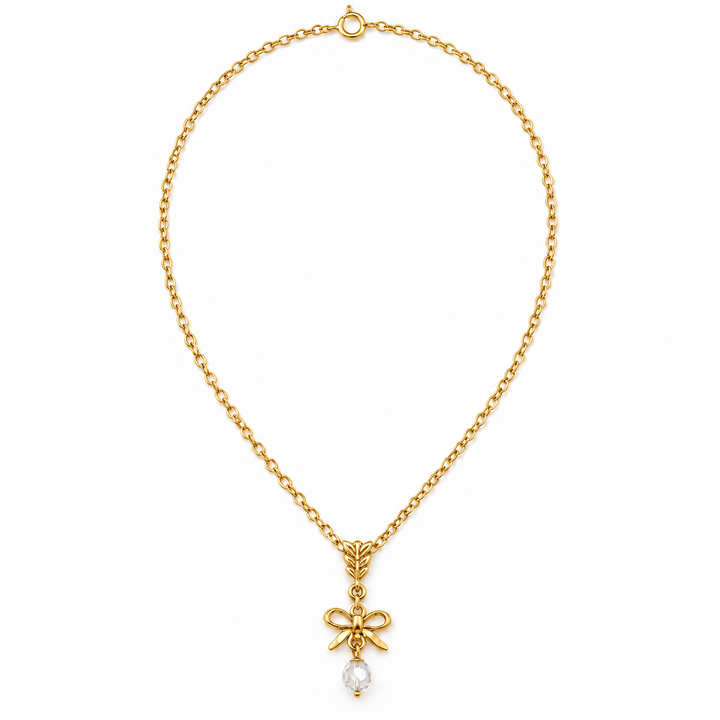 A gold chain necklace with a bow-shaped pendant and a small clear teardrop gemstone, shown on a plain white background.