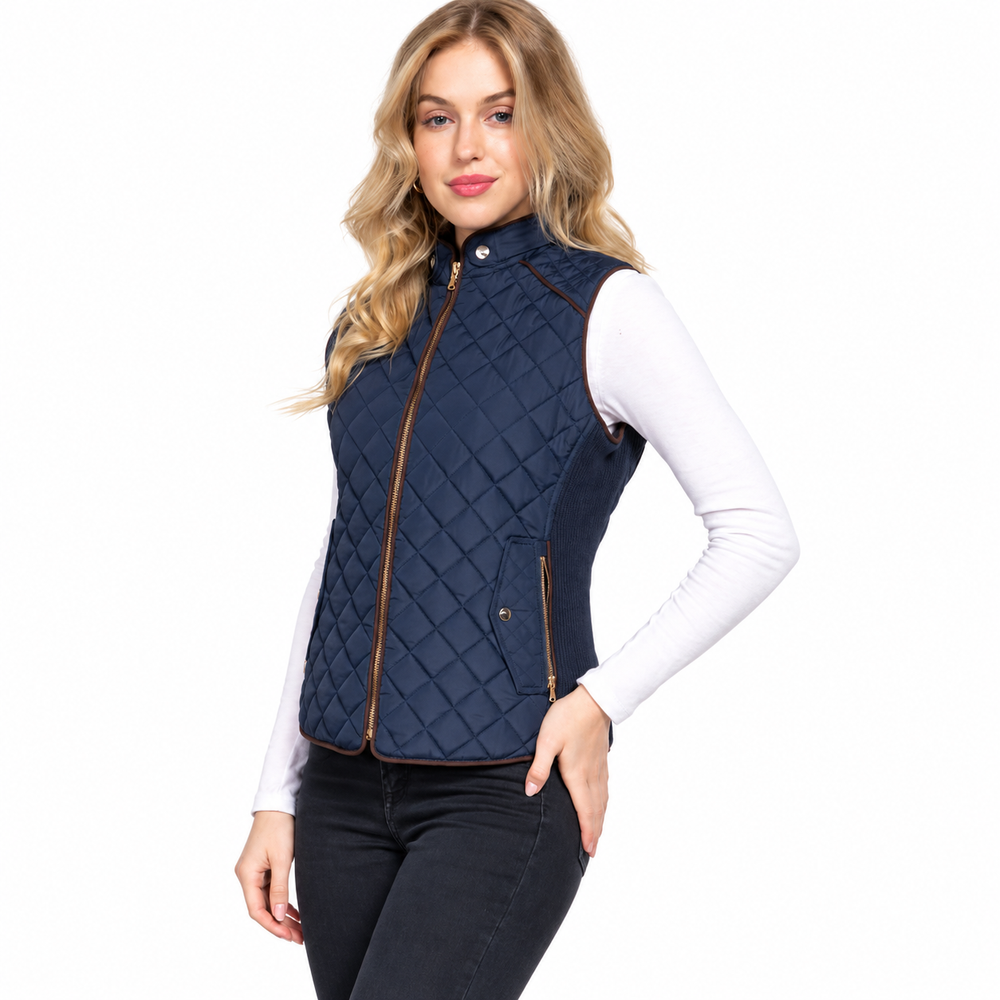 A woman modeling a sleeveless navy blue quilted vest with brown trim over a white long-sleeve top and black jeans, against a plain white background.