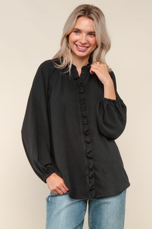 Woman wearing a black blouse with long sleeves and a ruffled collar against a beige background