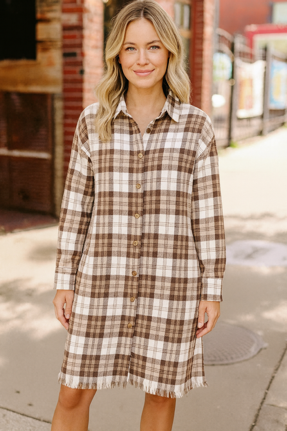 Woman wearing a plaid dress standing on a sidewalk with a brick building in the background