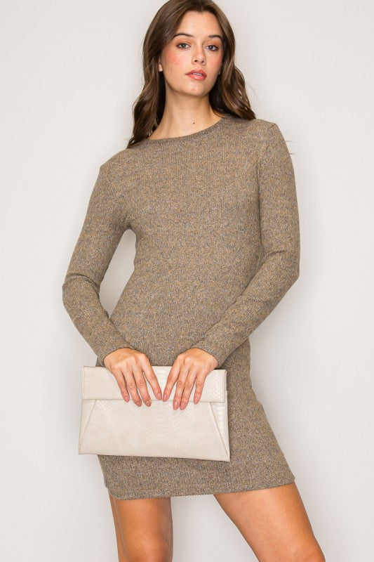 Woman wearing a brown sweater dress holding a white clutch against a plain background