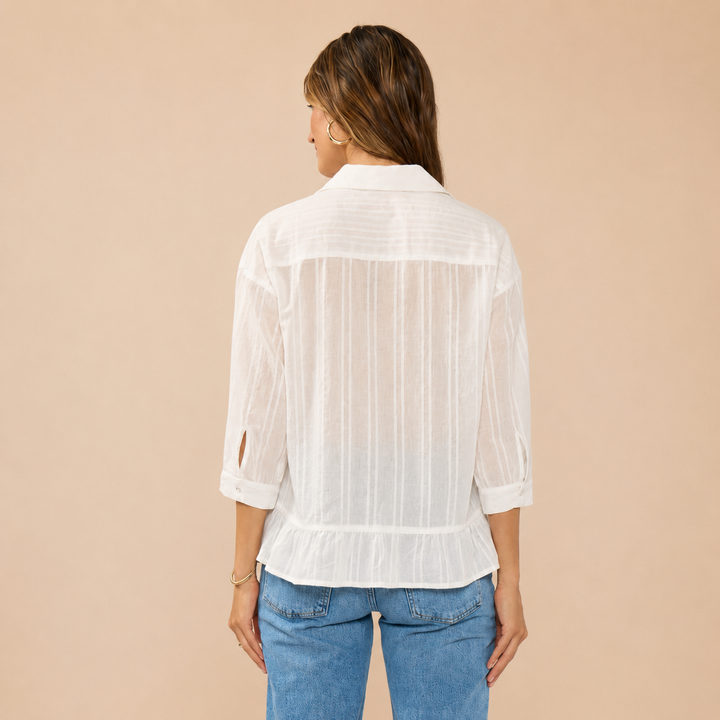 Woman wearing a white sheer blouse and blue jeans on a beige background