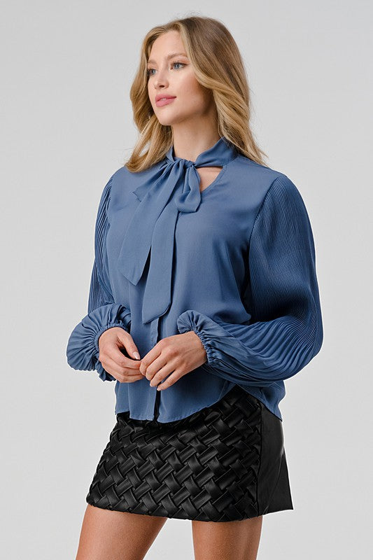Woman wearing a blue blouse with a tie neckline and a black woven skirt on a gray background