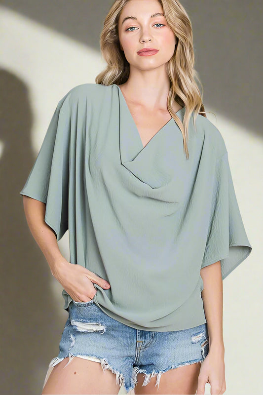 Woman wearing a light sage blouse denim shorts on a beige background