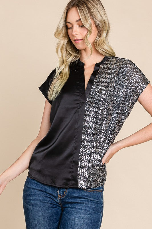 Woman wearing a black and silver sequin top with blue jeans on a beige background