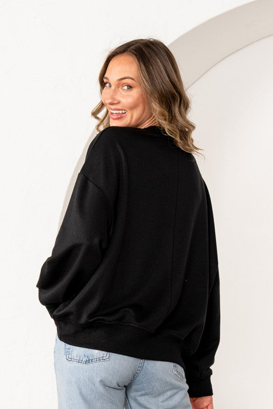 Woman wearing a black oversized sweater and light blue jeans against a white background