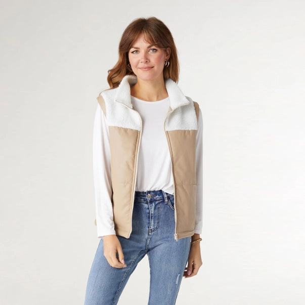 Woman wearing a white and beige fleece vest on a plain background